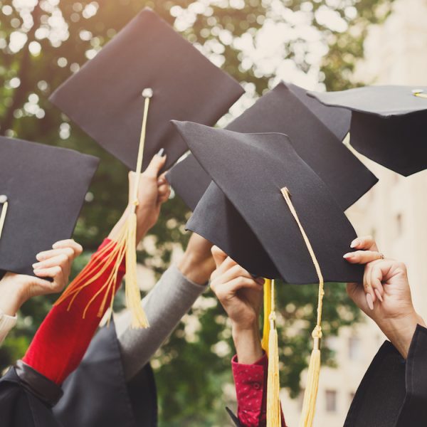 A group of multietnic students celebrating their graduation by throwing caps in the air closeup. Education, qualification and gown concept.