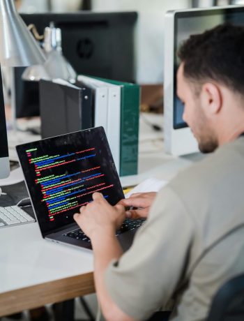 Focused software developer typing code on a laptop in a modern office setting.